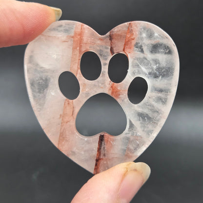 Fingers holding a heart carving with a paw print on a black background