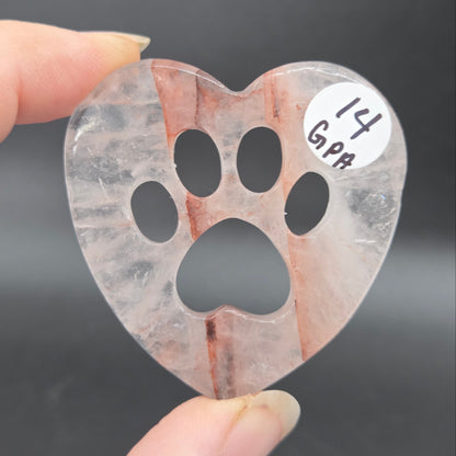 Fingers holding a heart carving with a paw print on a black background