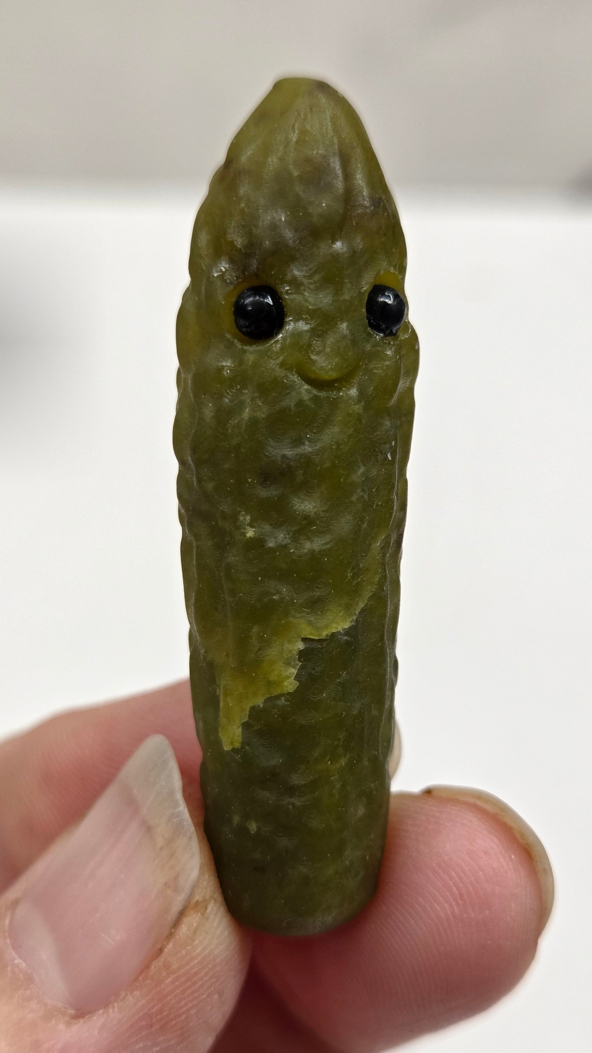 Hand holding a green jade pickle carving with black eye on a white background