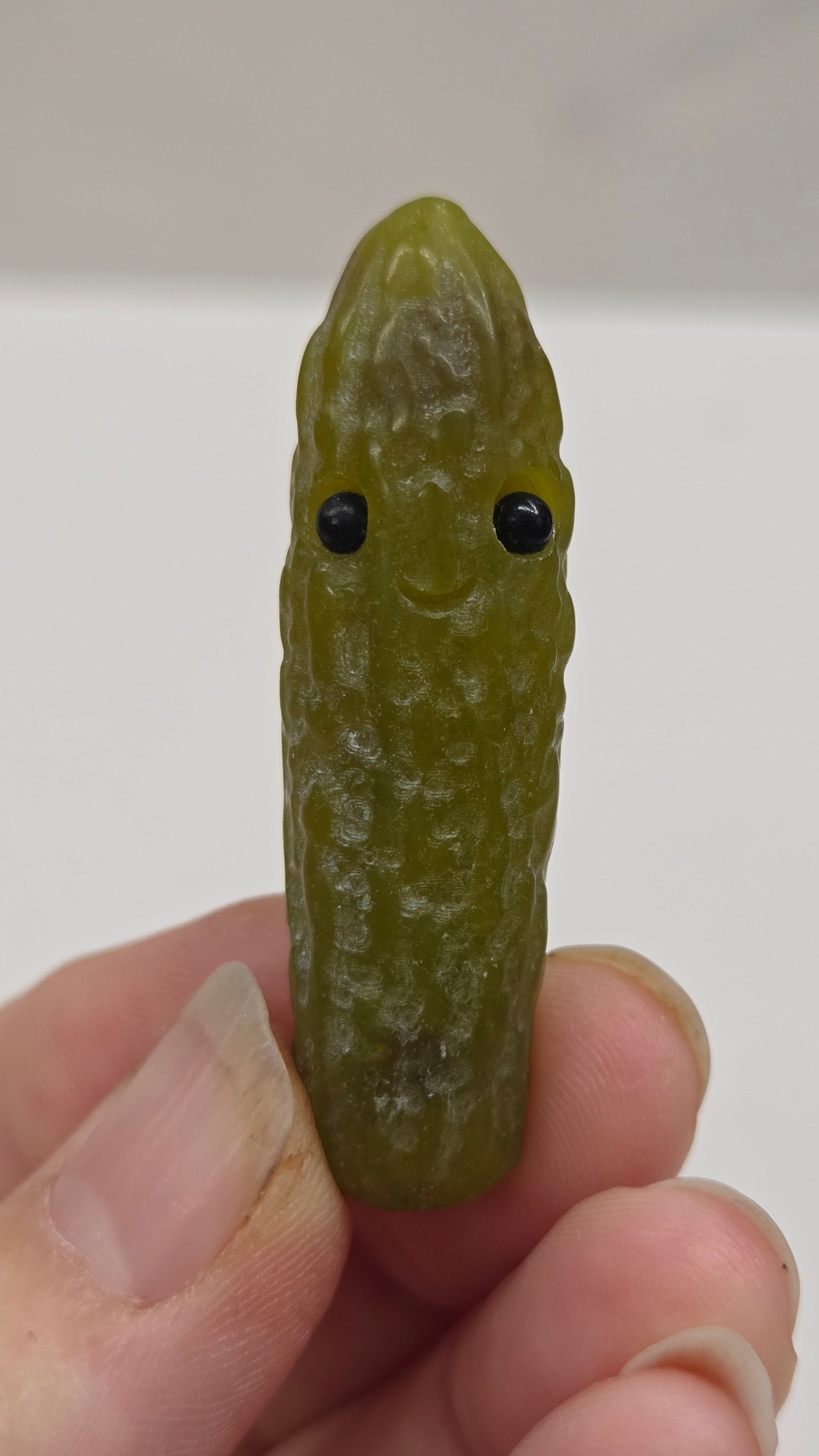 Hand holding a green jade pickle carving with black eye on a white background