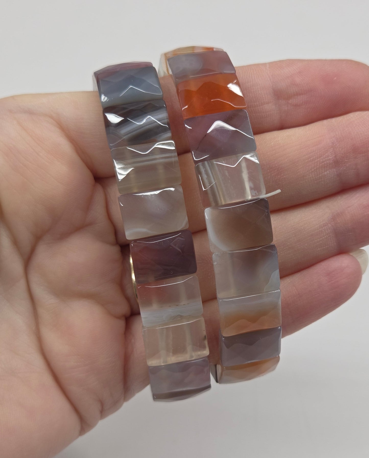 Hand holding a set of square-shaped, multicolored stone bracelets against a plain background.