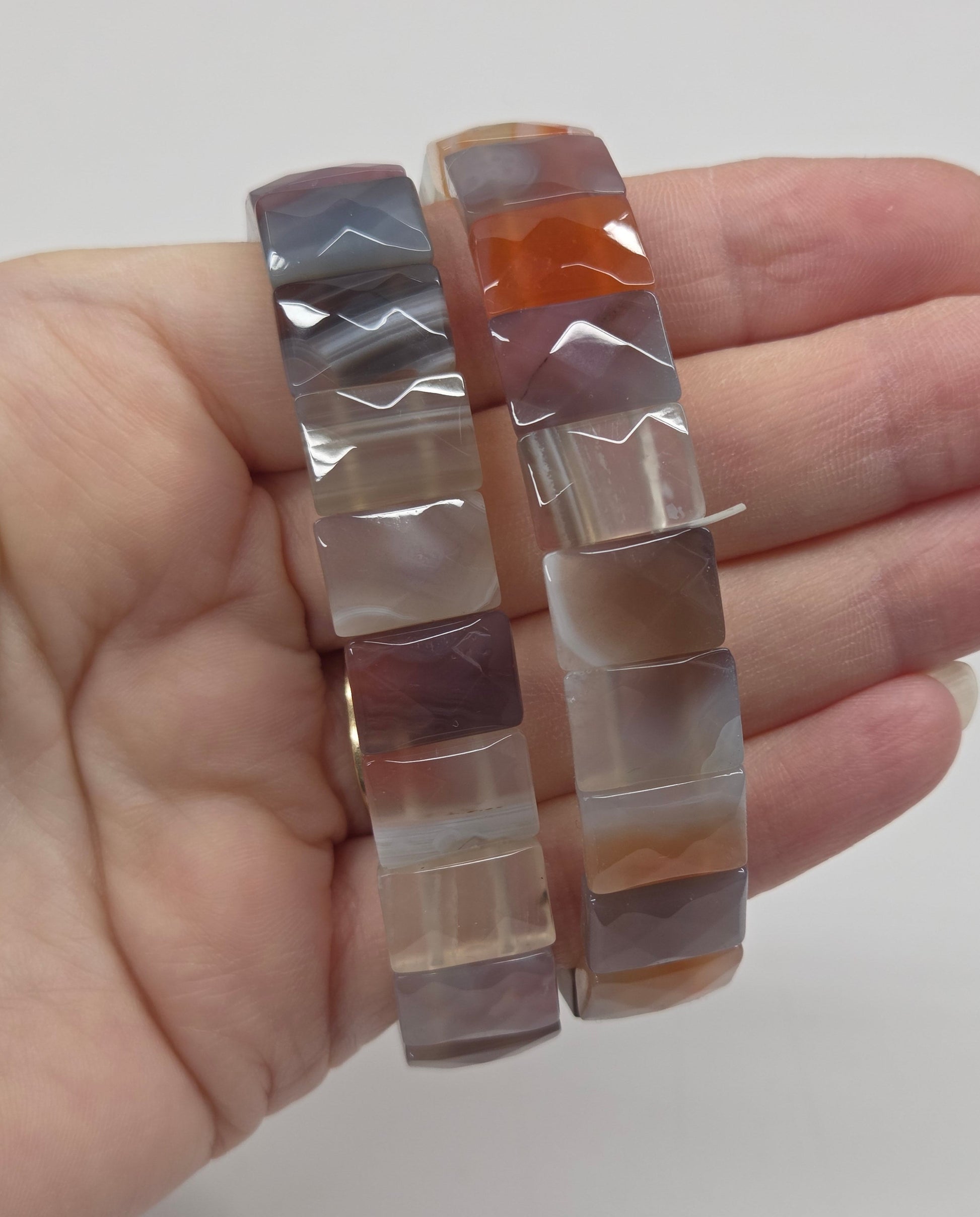 Hand holding a set of square-shaped, multicolored stone bracelets against a plain background.