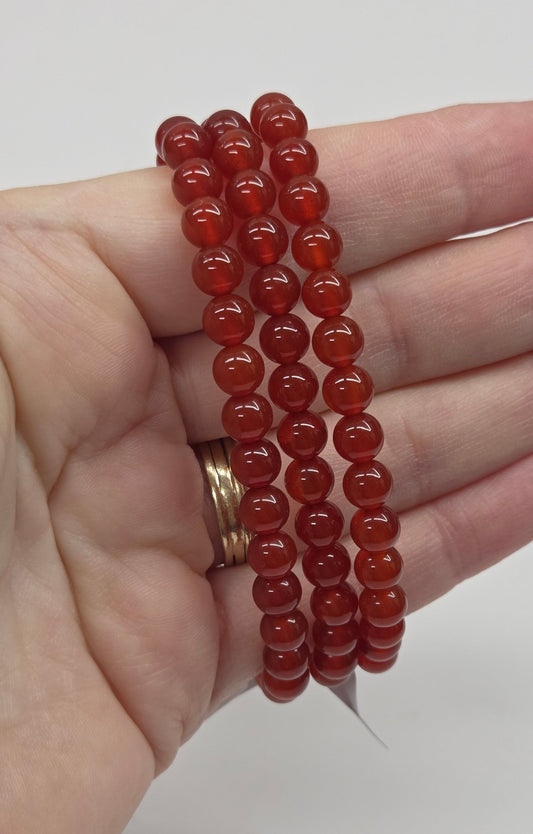 Hand holding a stack of red beaded bracelets against a white background
