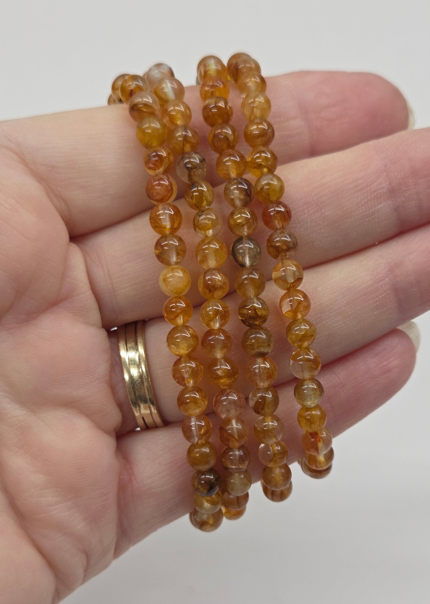 Hand wearing golden healer beaded bracelets on a plain background