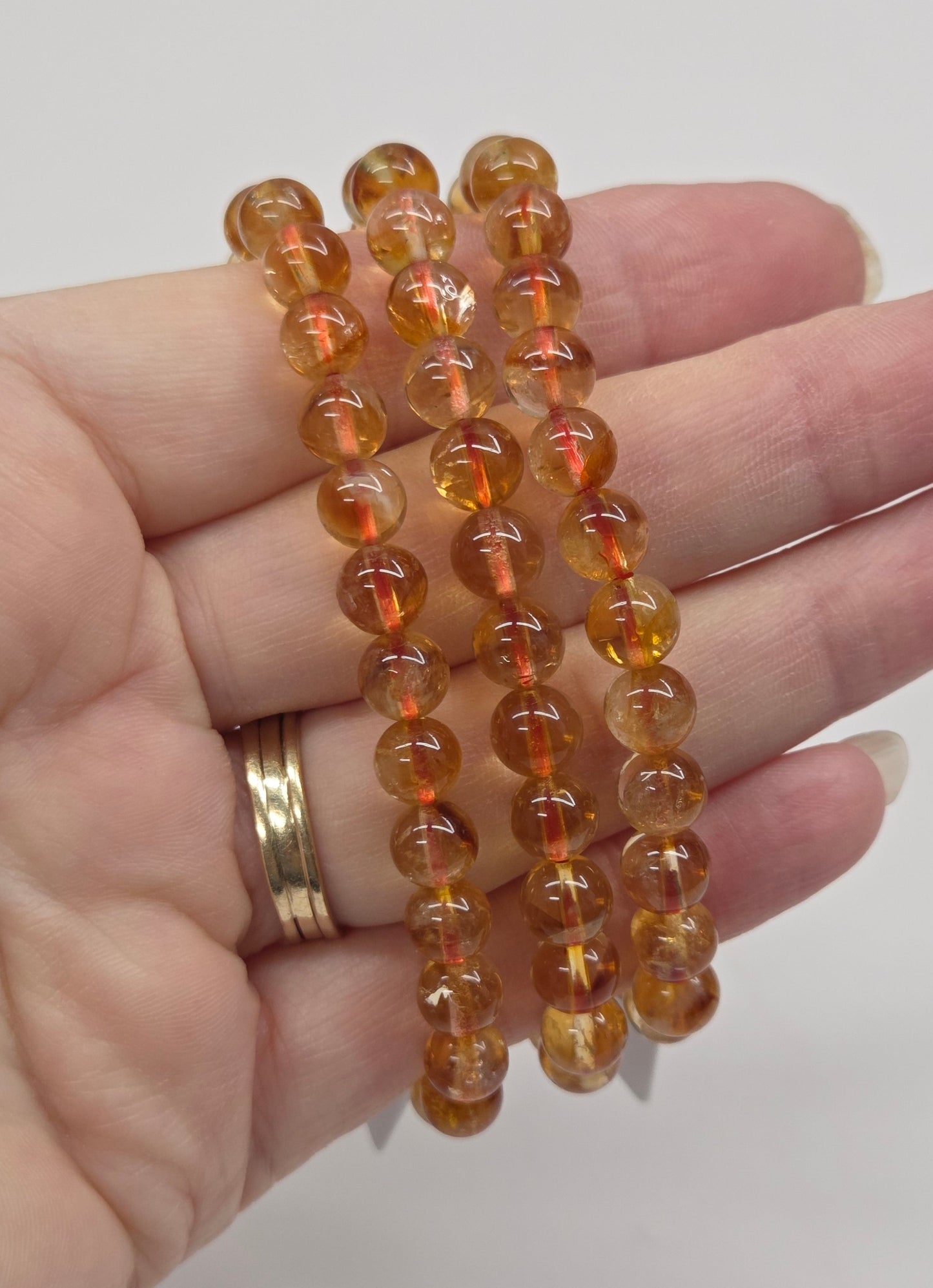 Hand wearing a stack of amber-colored beaded bracelets on a plain background