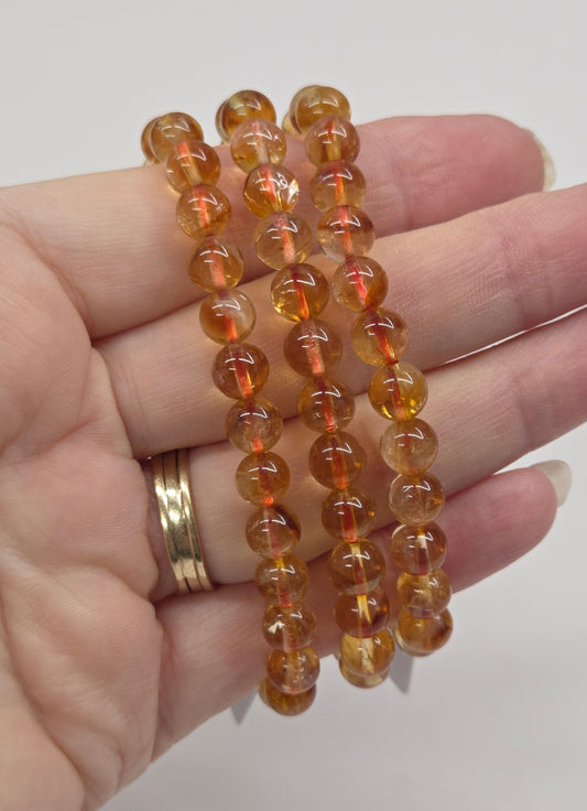 Hand wearing a stack of amber-colored beaded bracelets on a plain background
