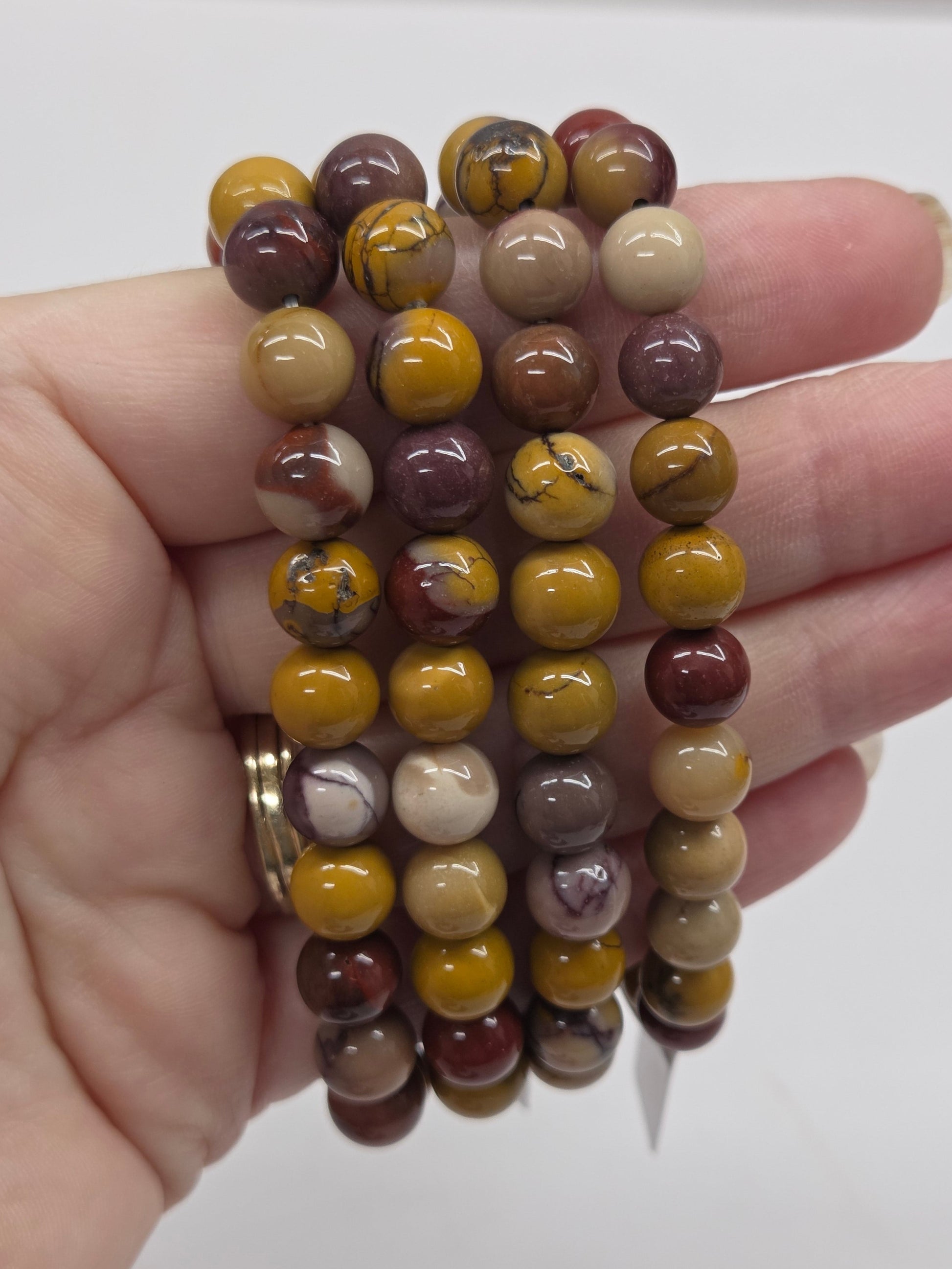 Hand holding a stack of multicolored beaded bracelets against a plain background