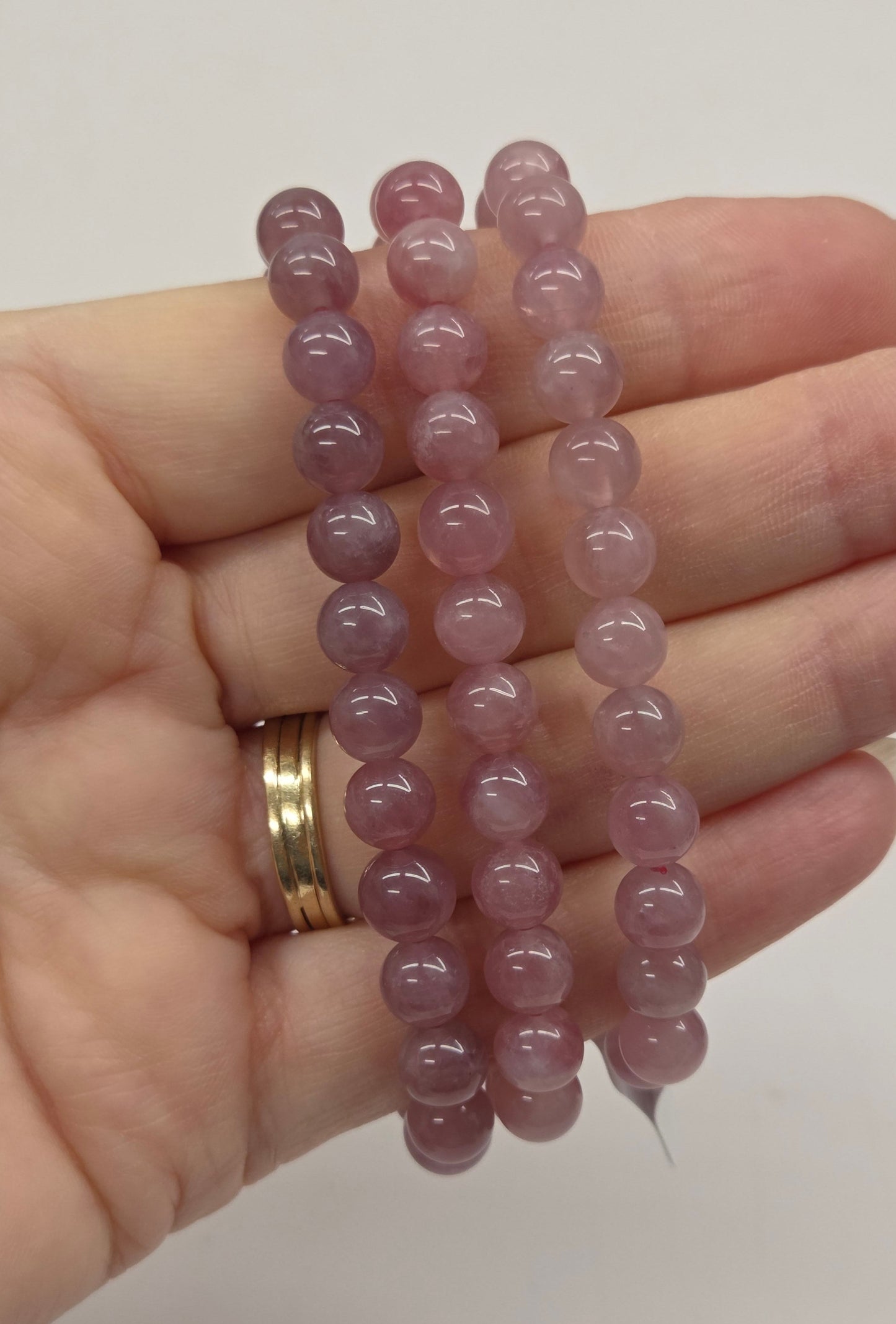 Hand holding three pink beaded bracelets against a plain background