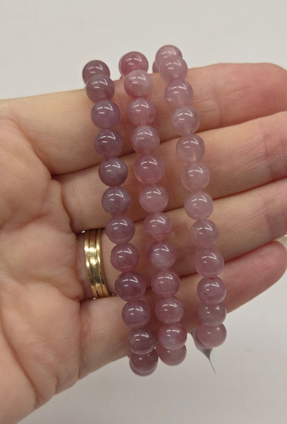 Hand holding three pink beaded bracelets against a plain background