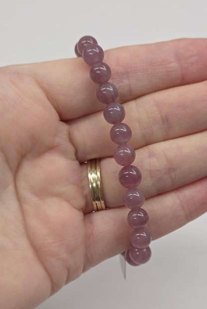 Hand wearing a pink beaded bracelet on a plain background