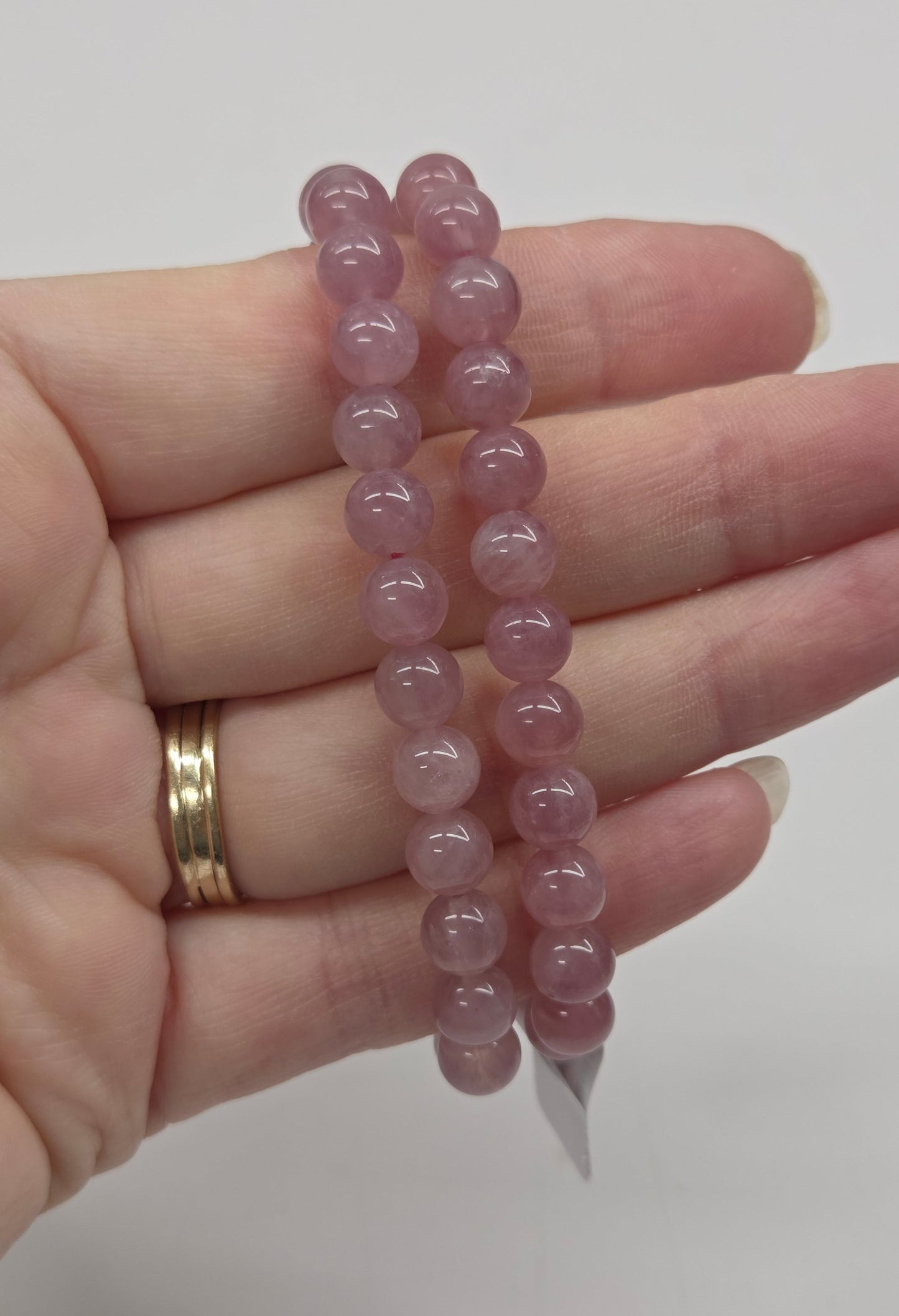 Hand wearing a pink beaded bracelet on a plain background
