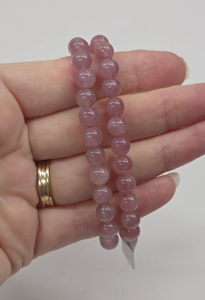 Hand wearing a pink beaded bracelet on a plain background