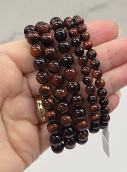 Hand holding a stack of brown beaded bracelets against a neutral background