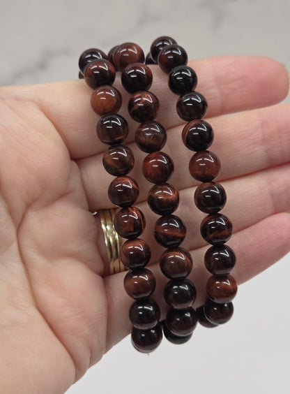 Hand holding three brown beaded bracelets against a neutral background