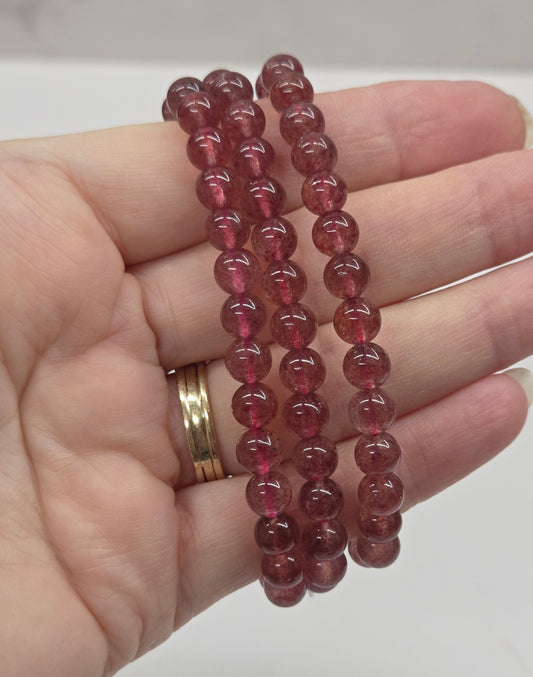 Hand wearing red beaded bracelets on a neutral background