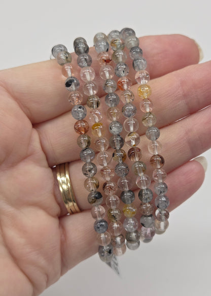 Hand wearing multiple beaded bracelets on a plain background
