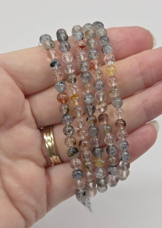 Hand wearing multiple beaded bracelets on a plain background