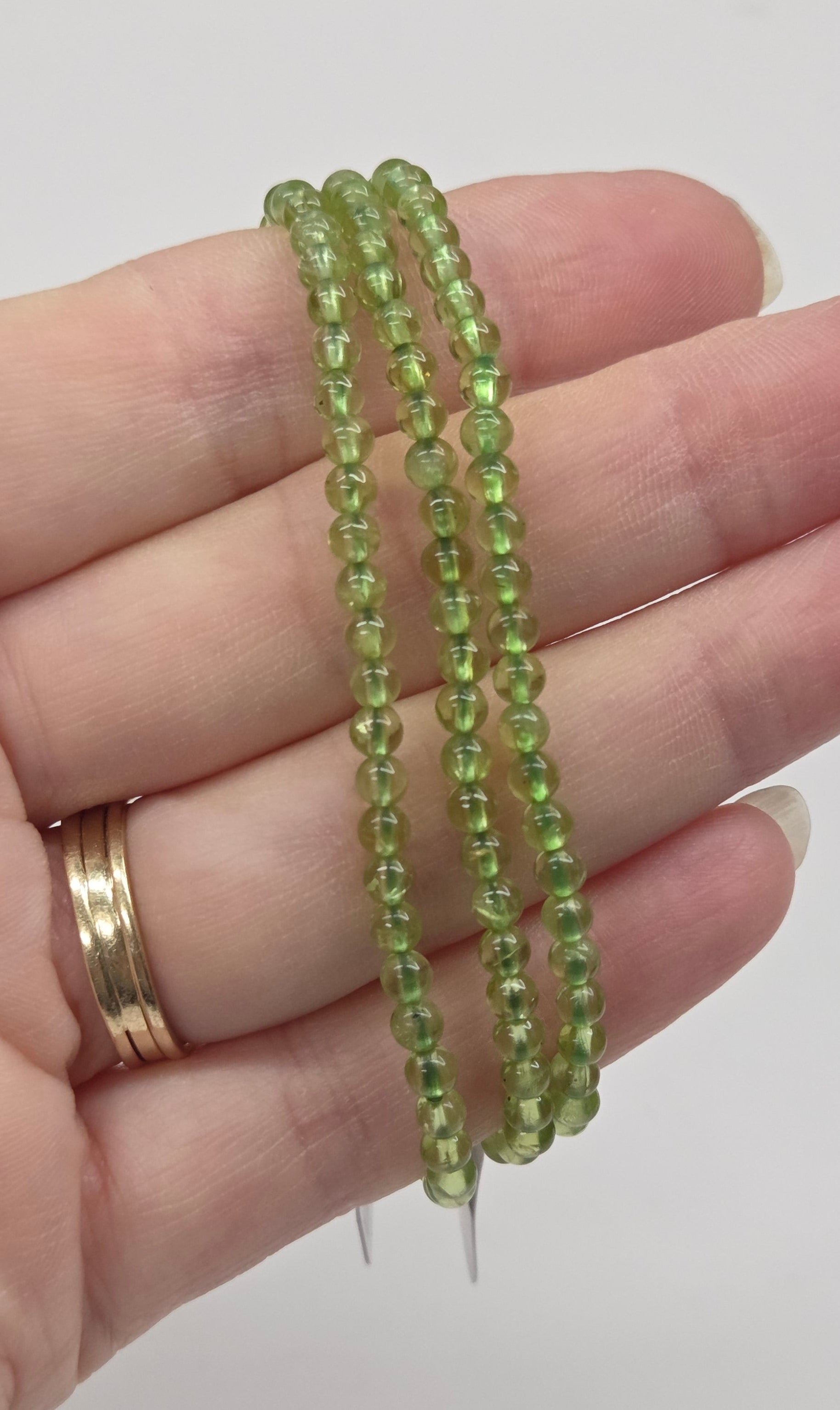 Hand wearing green beaded bracelets on a plain background