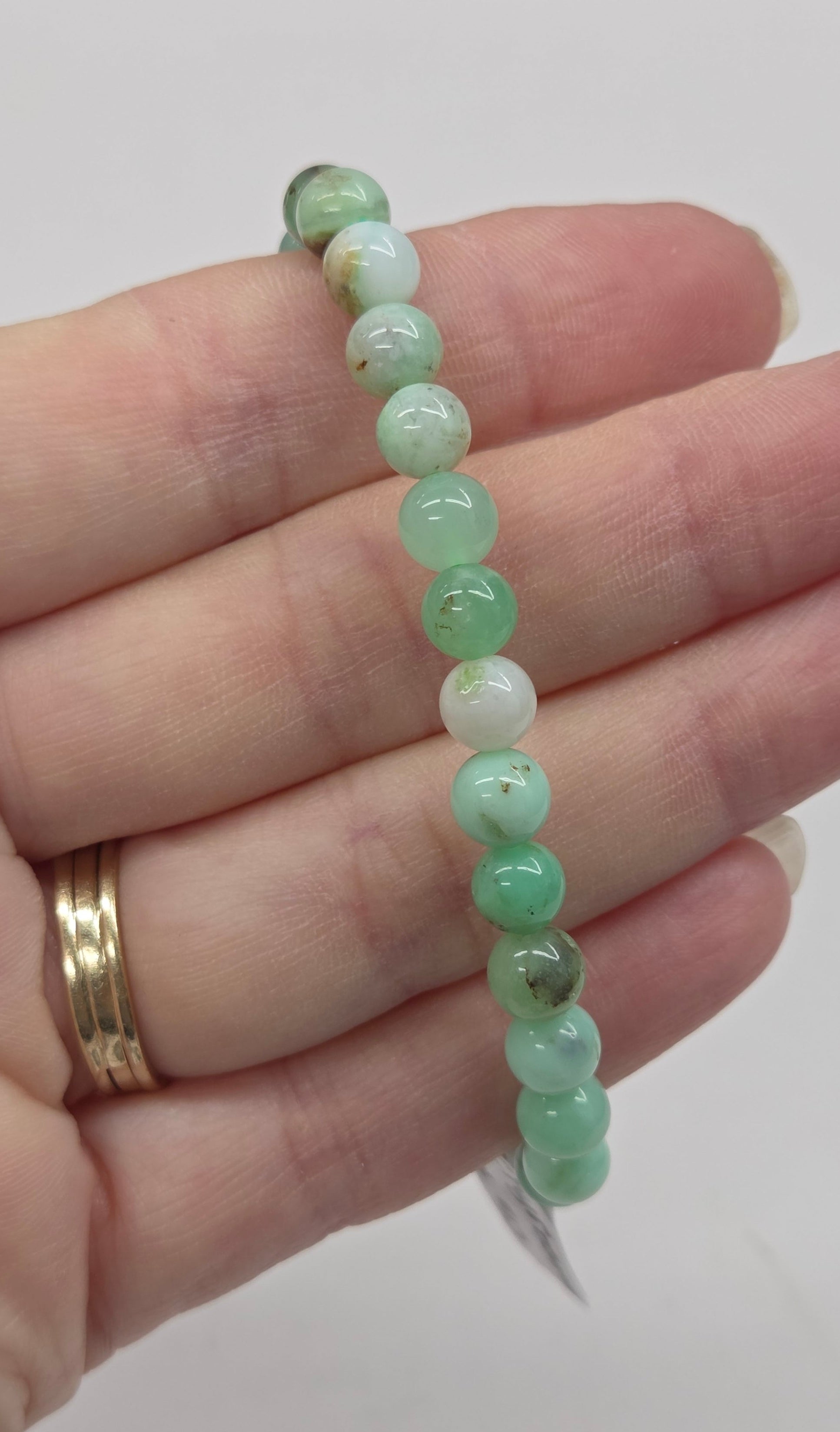 Hand holding a bracelet with green and white beads against a plain background