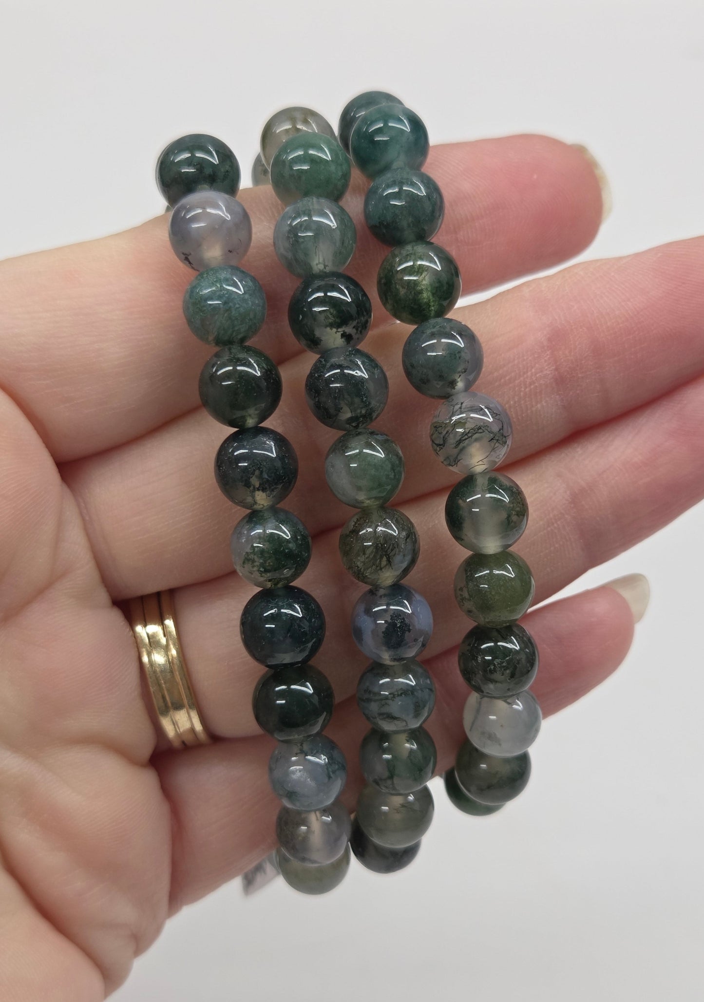 Hand wearing a stack of green beaded bracelets on a plain background