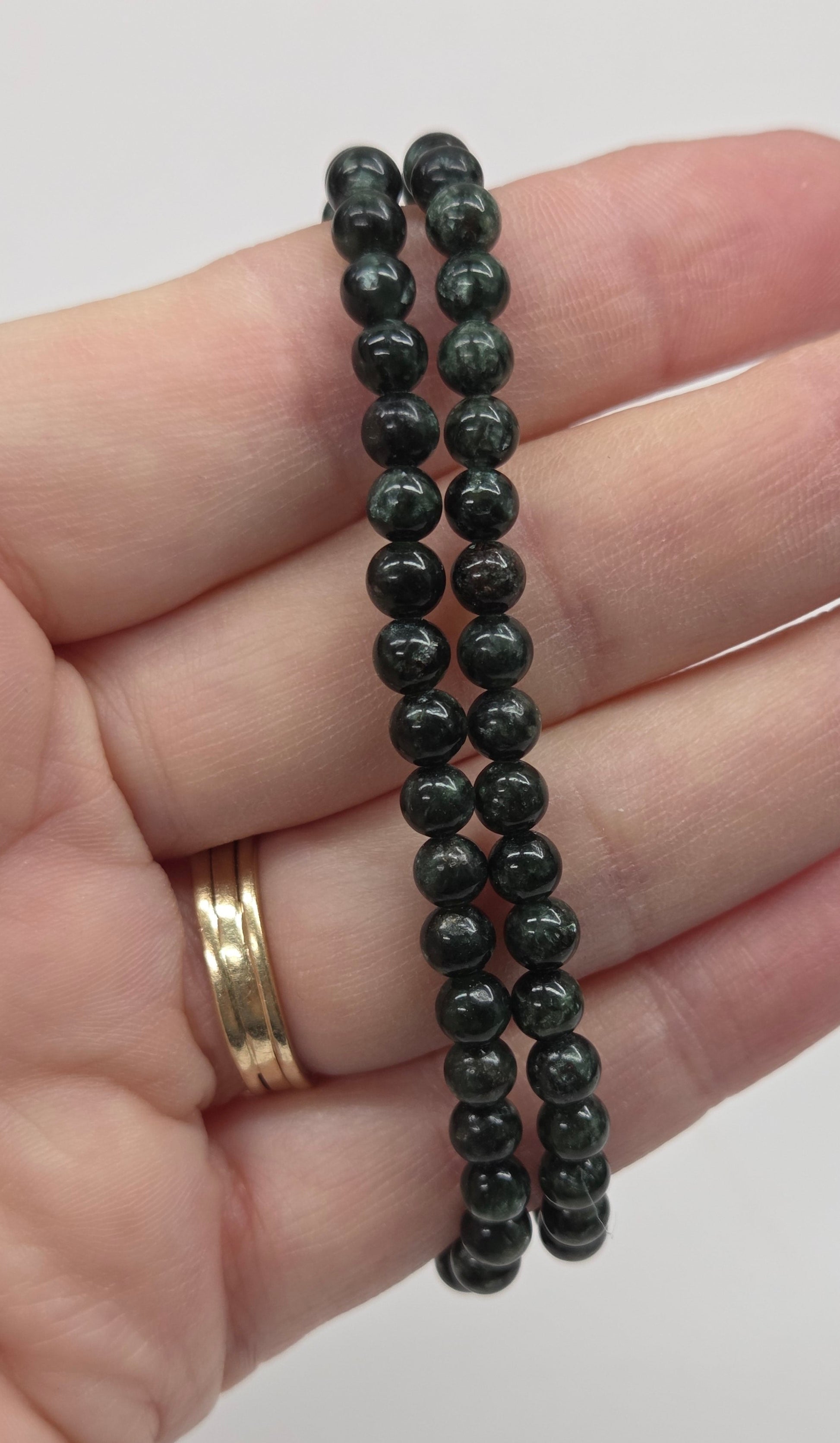 Hand wearing two black beaded bracelets on a plain background