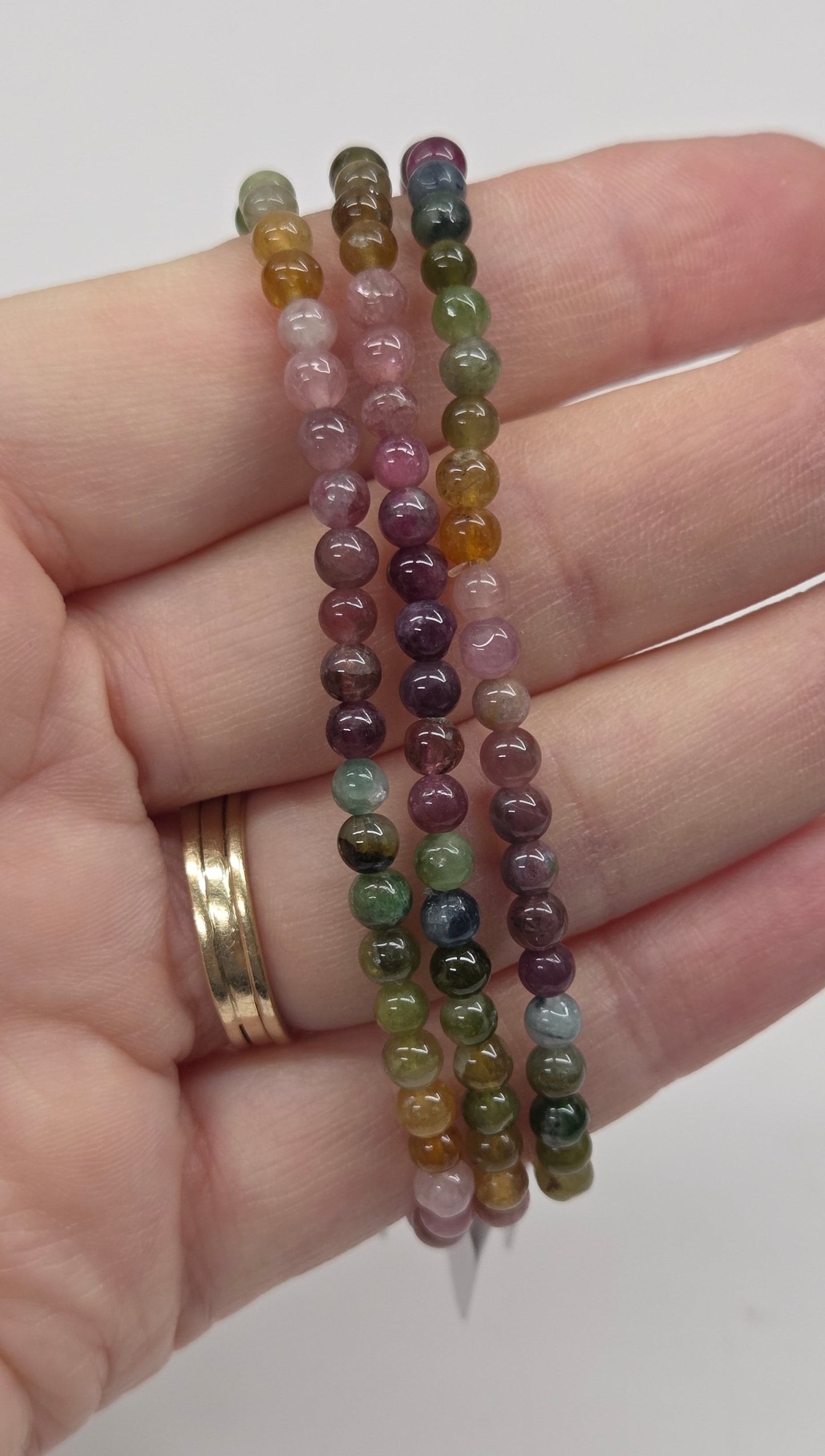 Hand wearing two beaded bracelets on a plain background