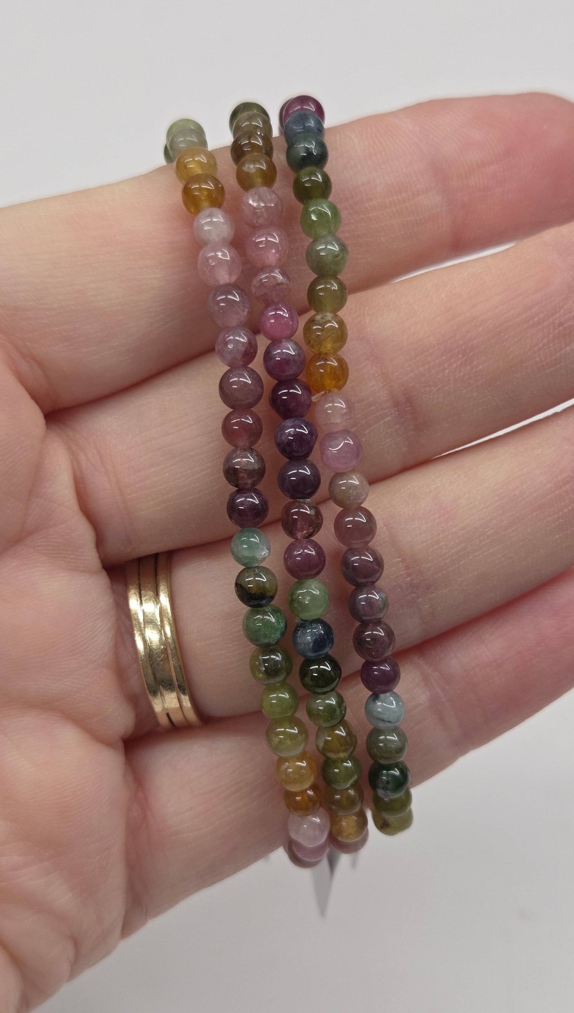 Hand wearing two beaded bracelets on a plain background