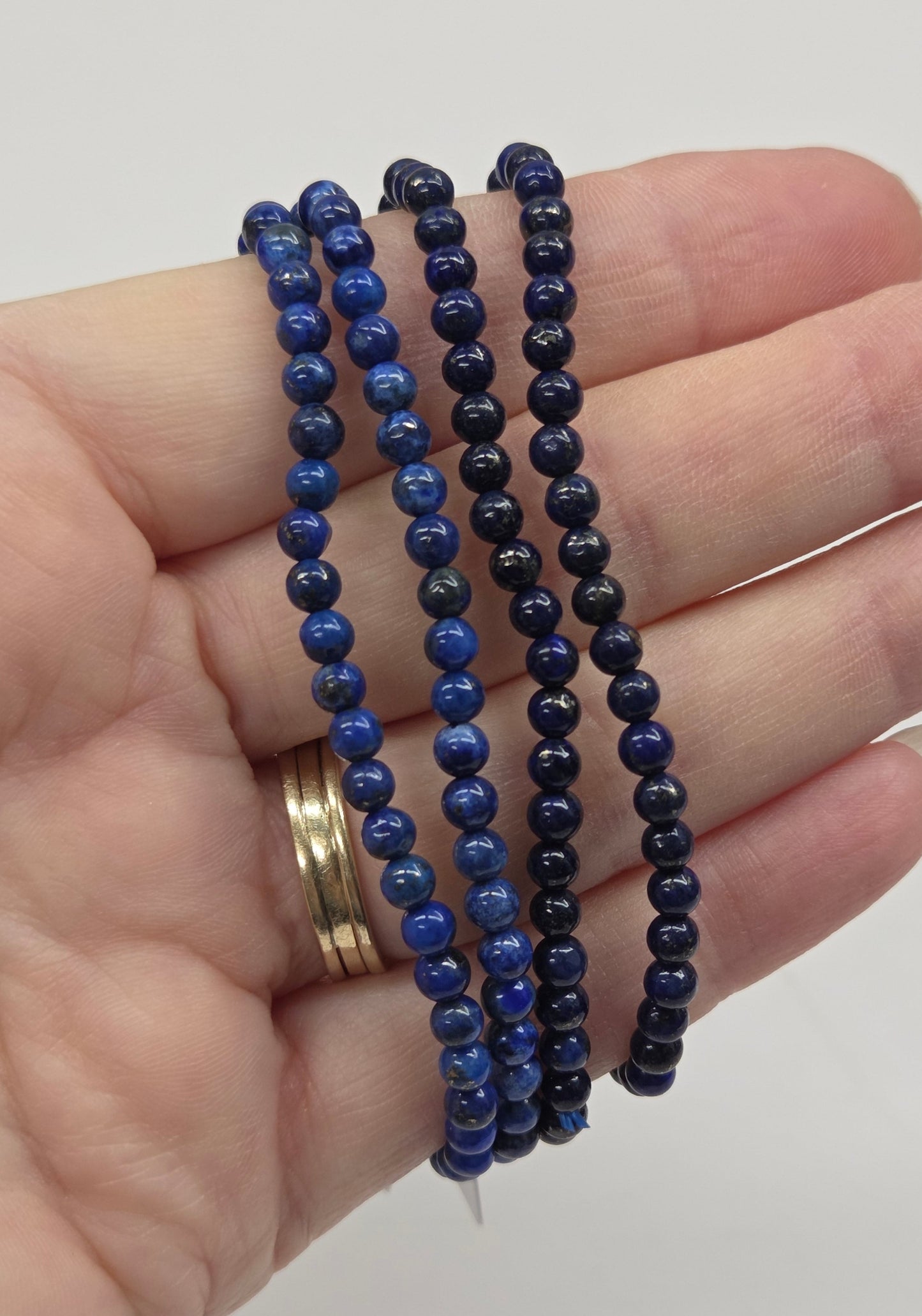 Hand wearing blue beaded bracelets on a plain background
