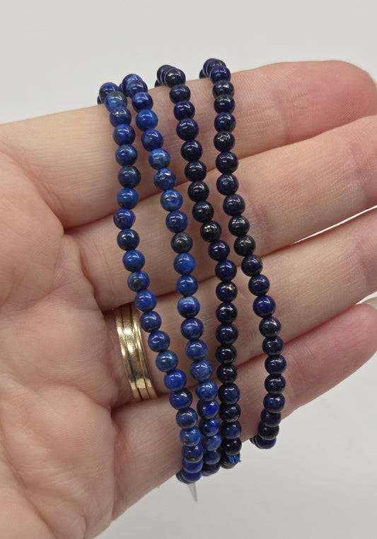 Hand wearing blue beaded bracelets on a plain background