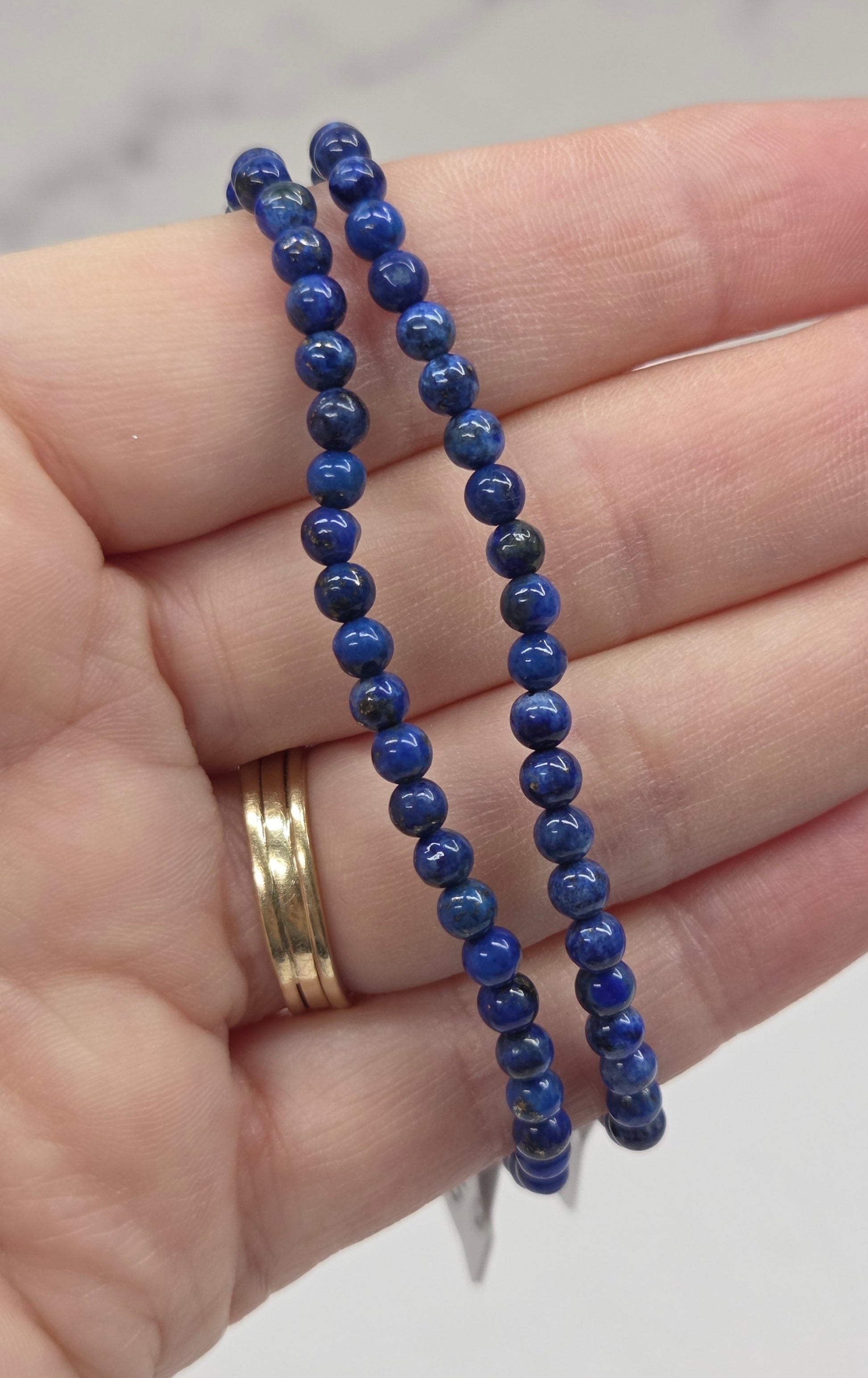 Hand wearing two blue beaded bracelets on a neutral background