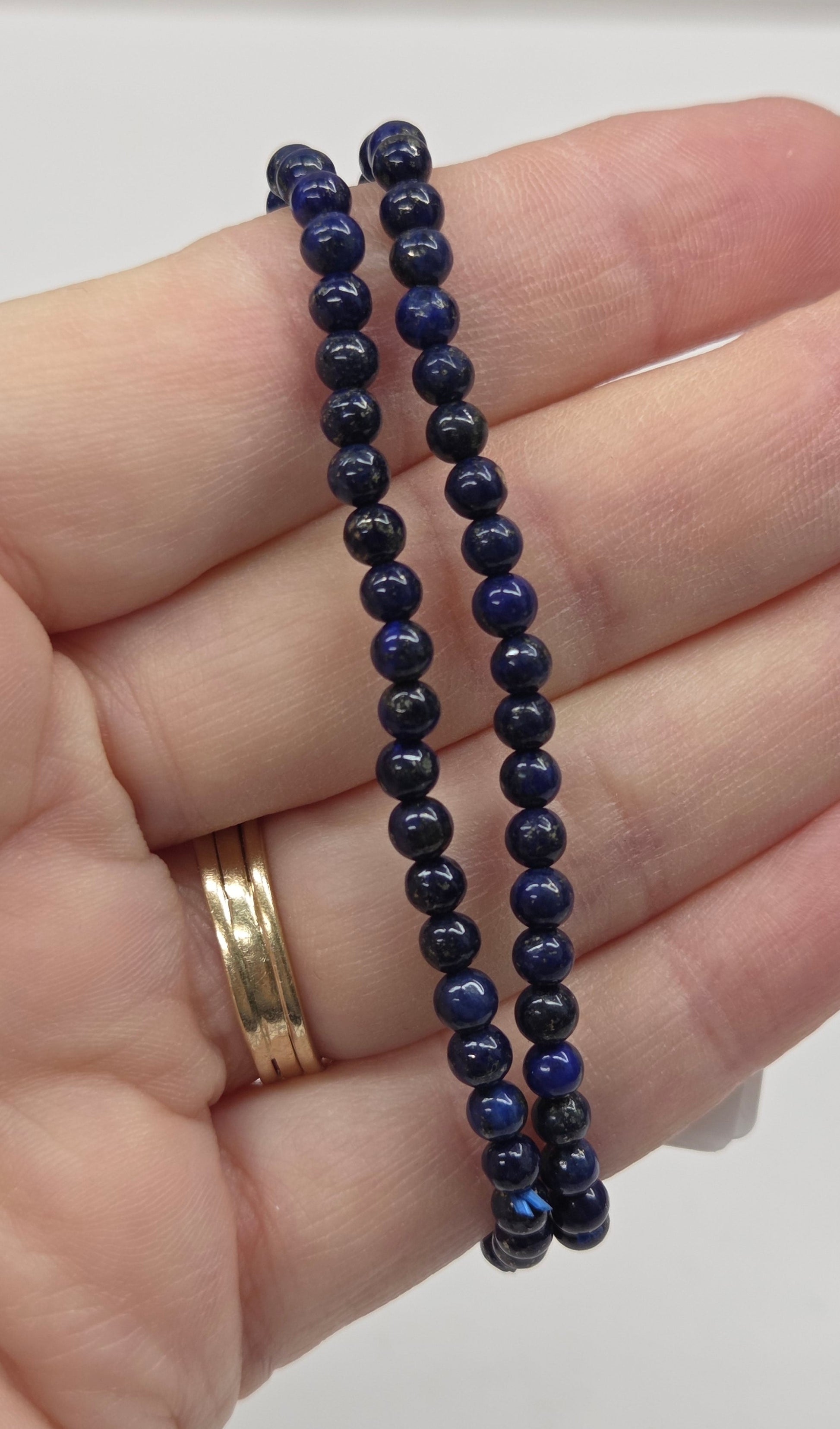 Hand wearing two dark blue beaded bracelets on a plain background