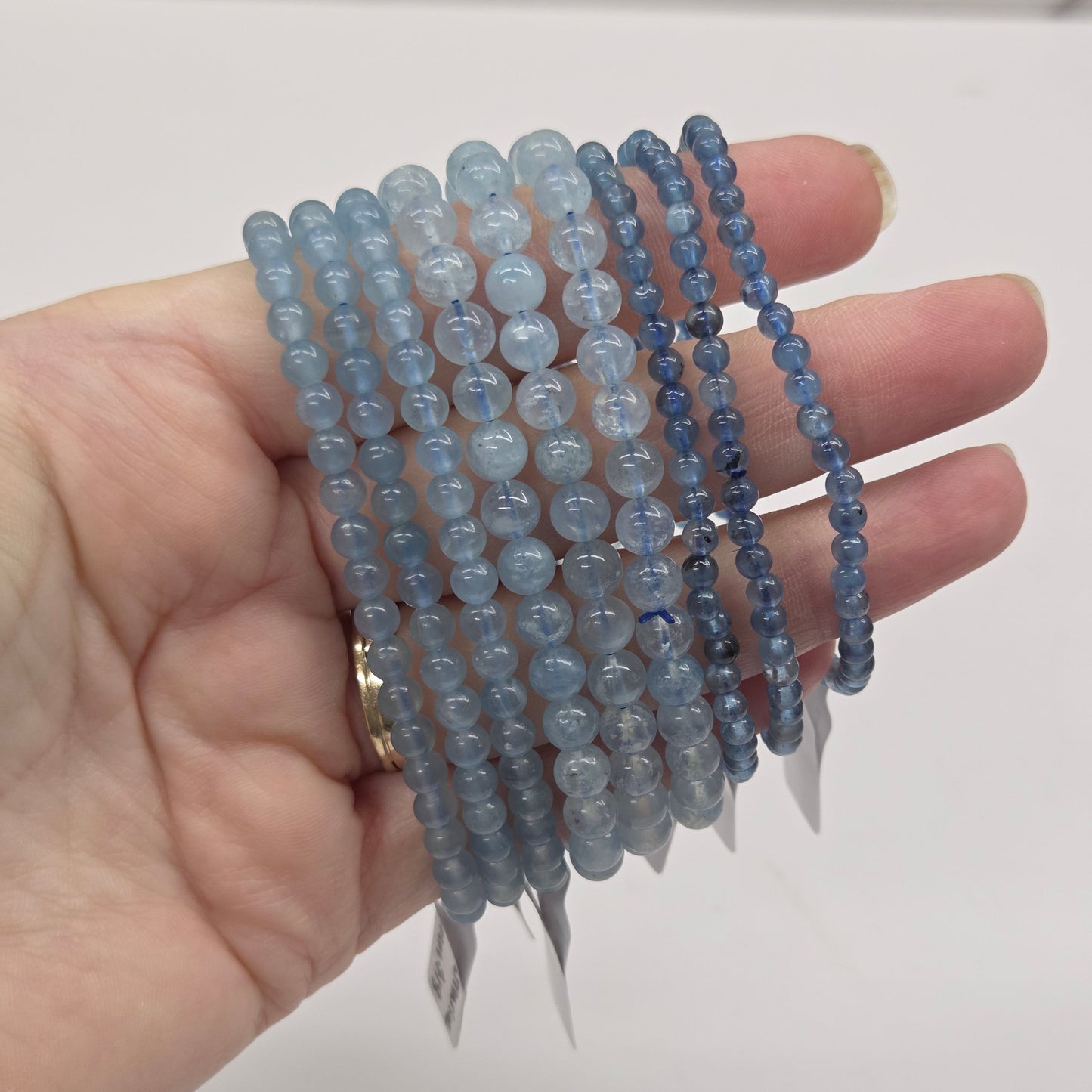 Hand wearing multiple blue beaded bracelets on a plain background