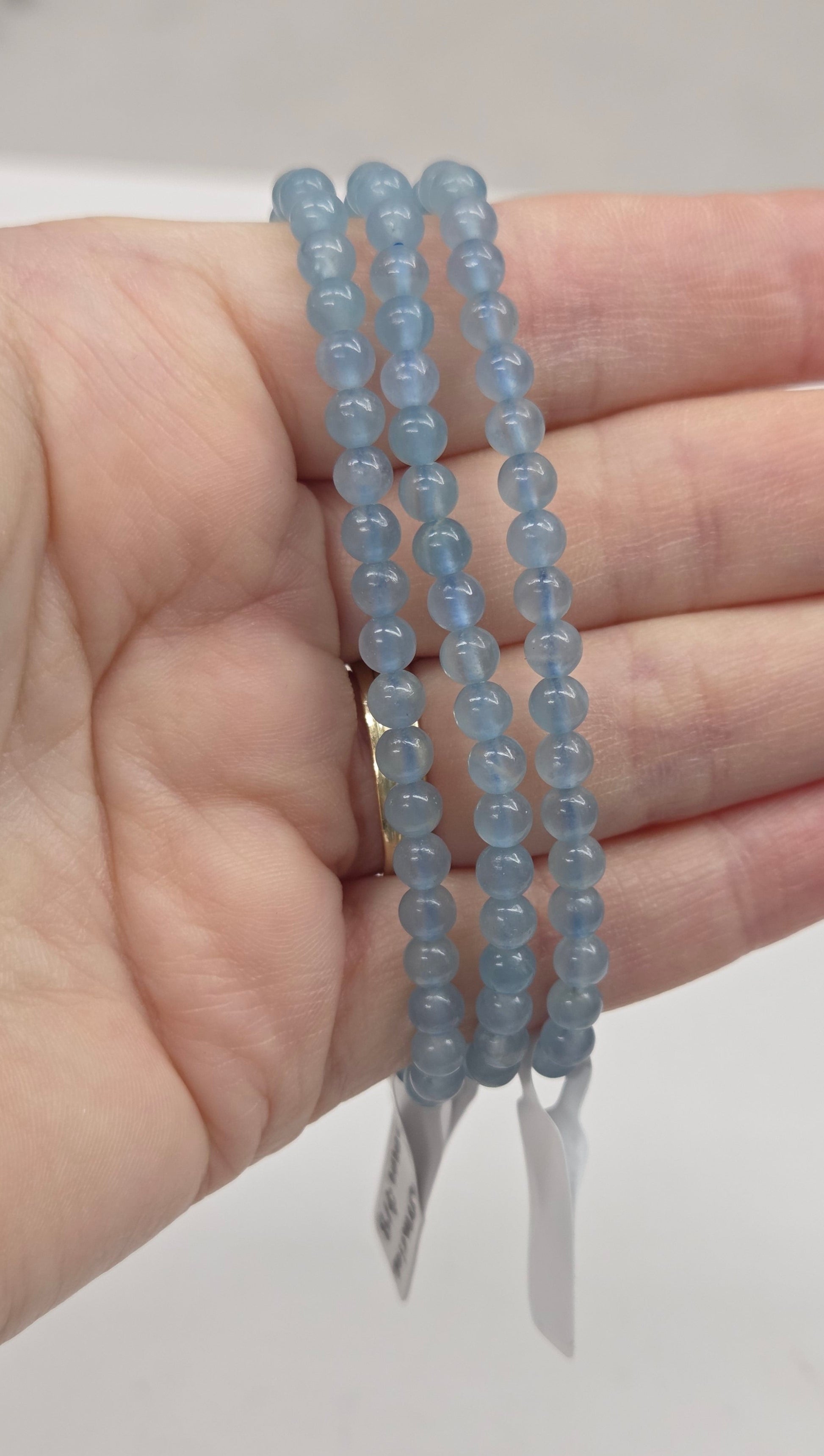 Hand holding three blue beaded bracelets against a neutral background