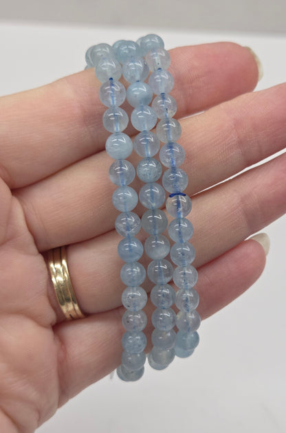 Hand holding three blue beaded bracelets against a white background