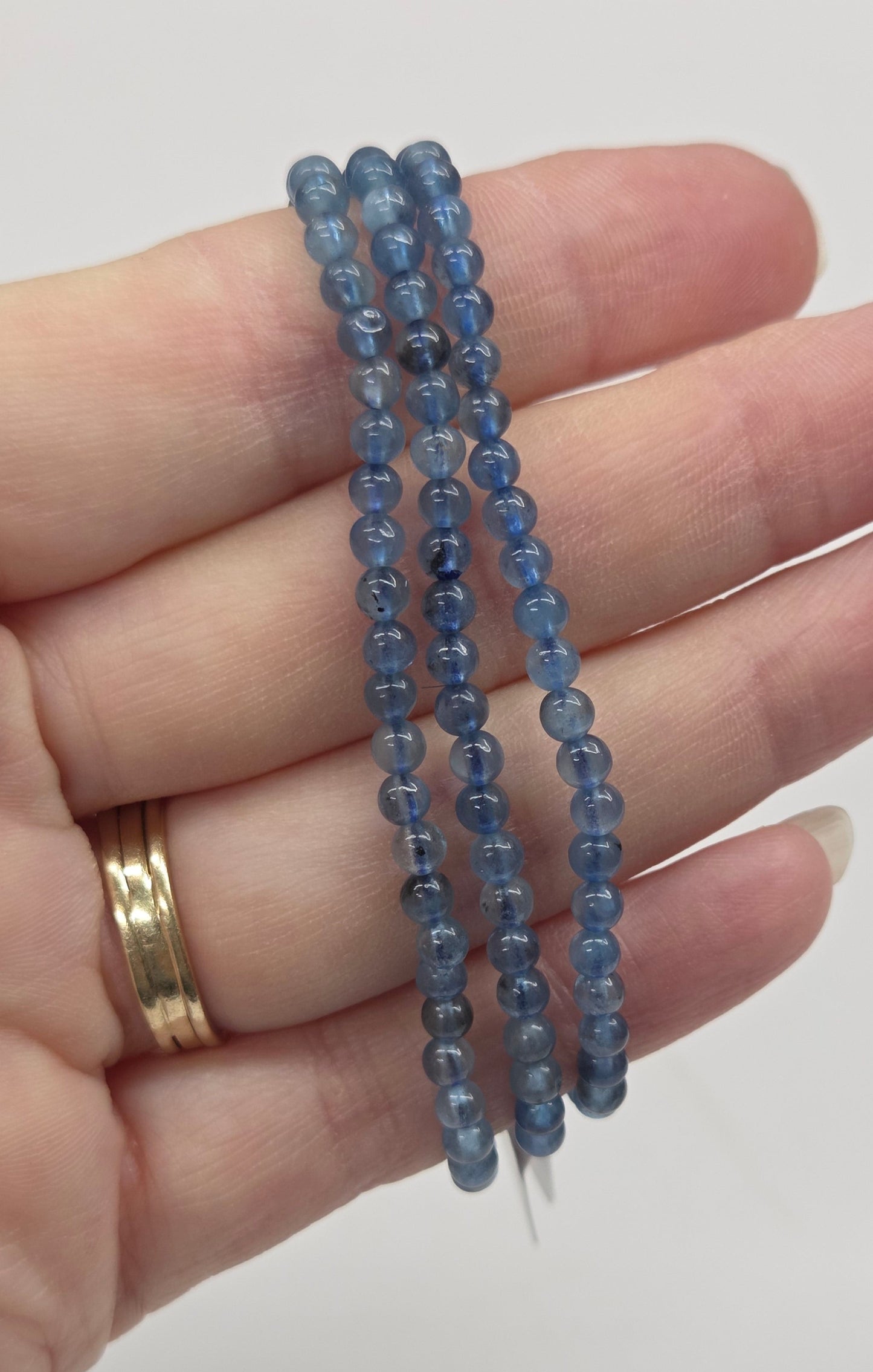Hand wearing three blue beaded bracelets on a plain background