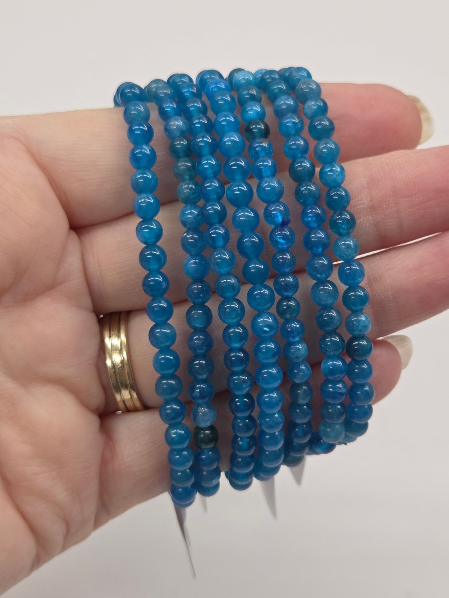 Hand holding multiple blue beaded bracelets against a plain background