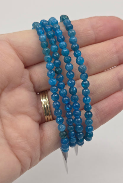 Hand wearing blue beaded bracelets on a plain background