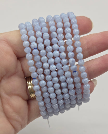 Hand holding multiple light blue beaded bracelets against a plain background