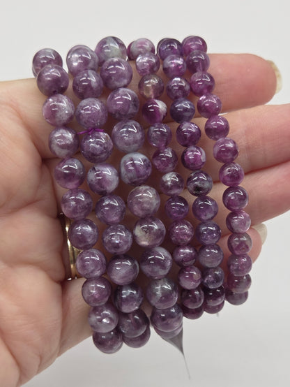 Hand holding multiple purple beaded bracelets against a white background