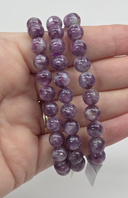 Purple beaded bracelets on a hand against a white background
