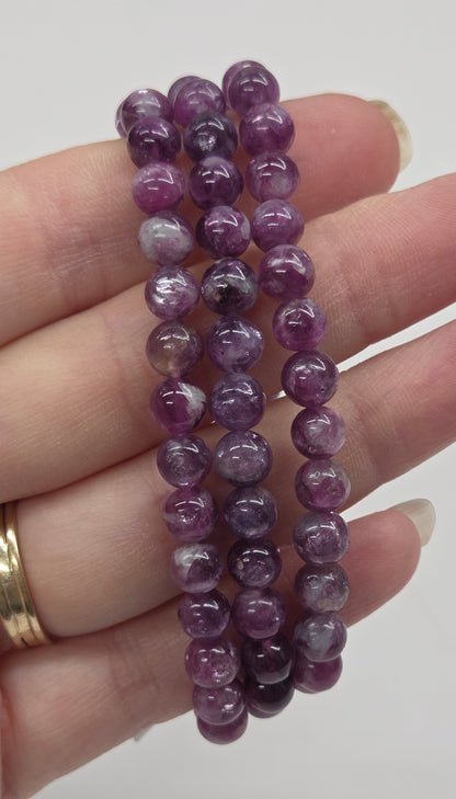 Purple beaded bracelets on a hand with a plain background