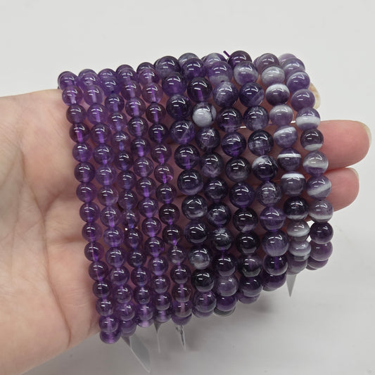 Hand holding a stack of purple beaded bracelets against a white background