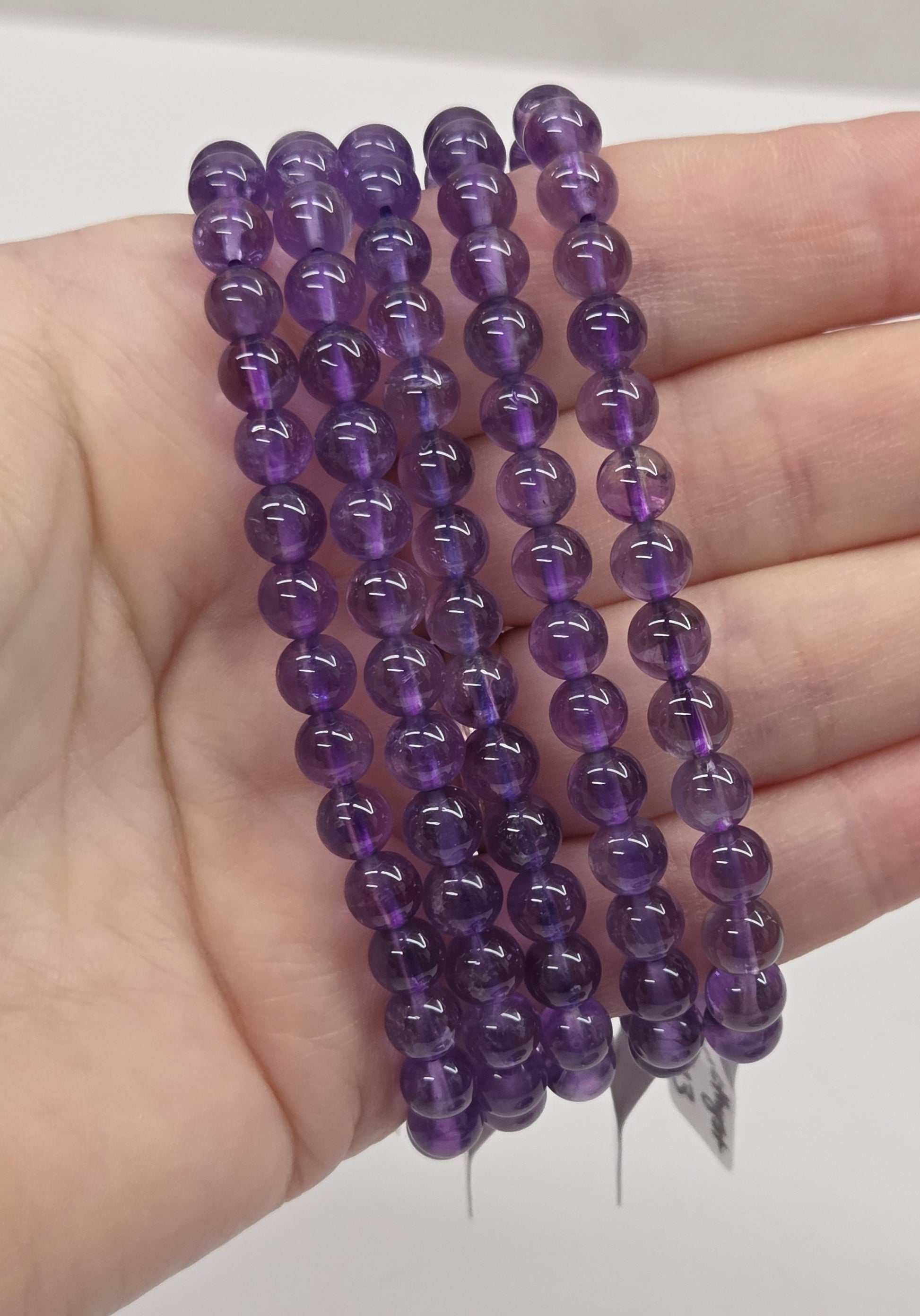 Hand holding three purple beaded bracelets against a white background