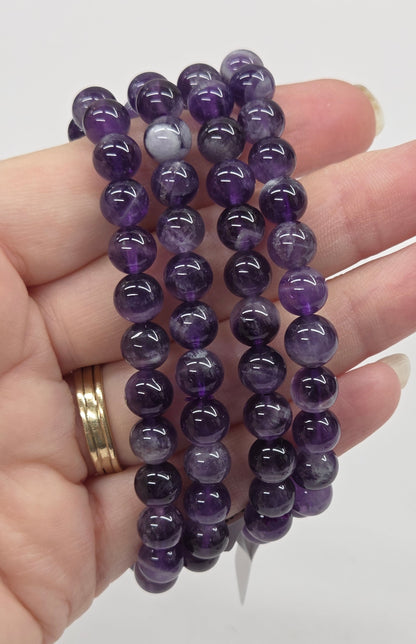 Hand holding purple beaded bracelets against a white background