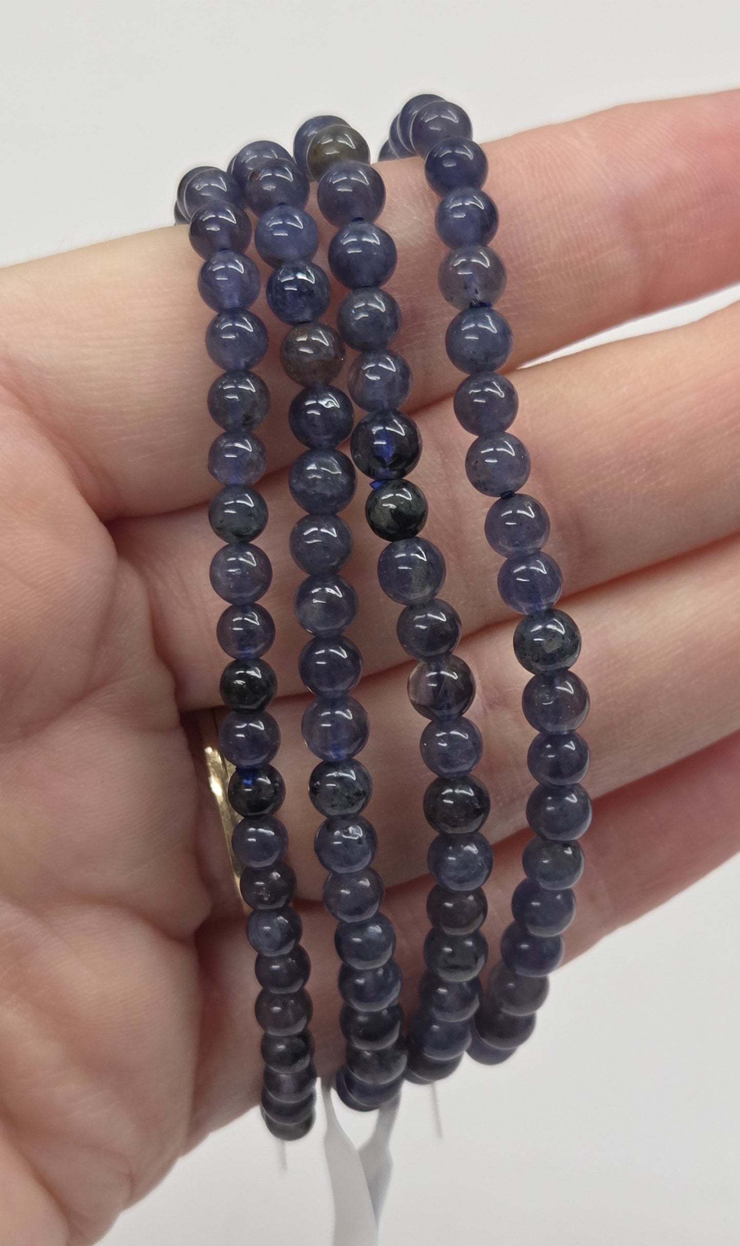 Four dark blue beaded bracelets on a hand against a light background