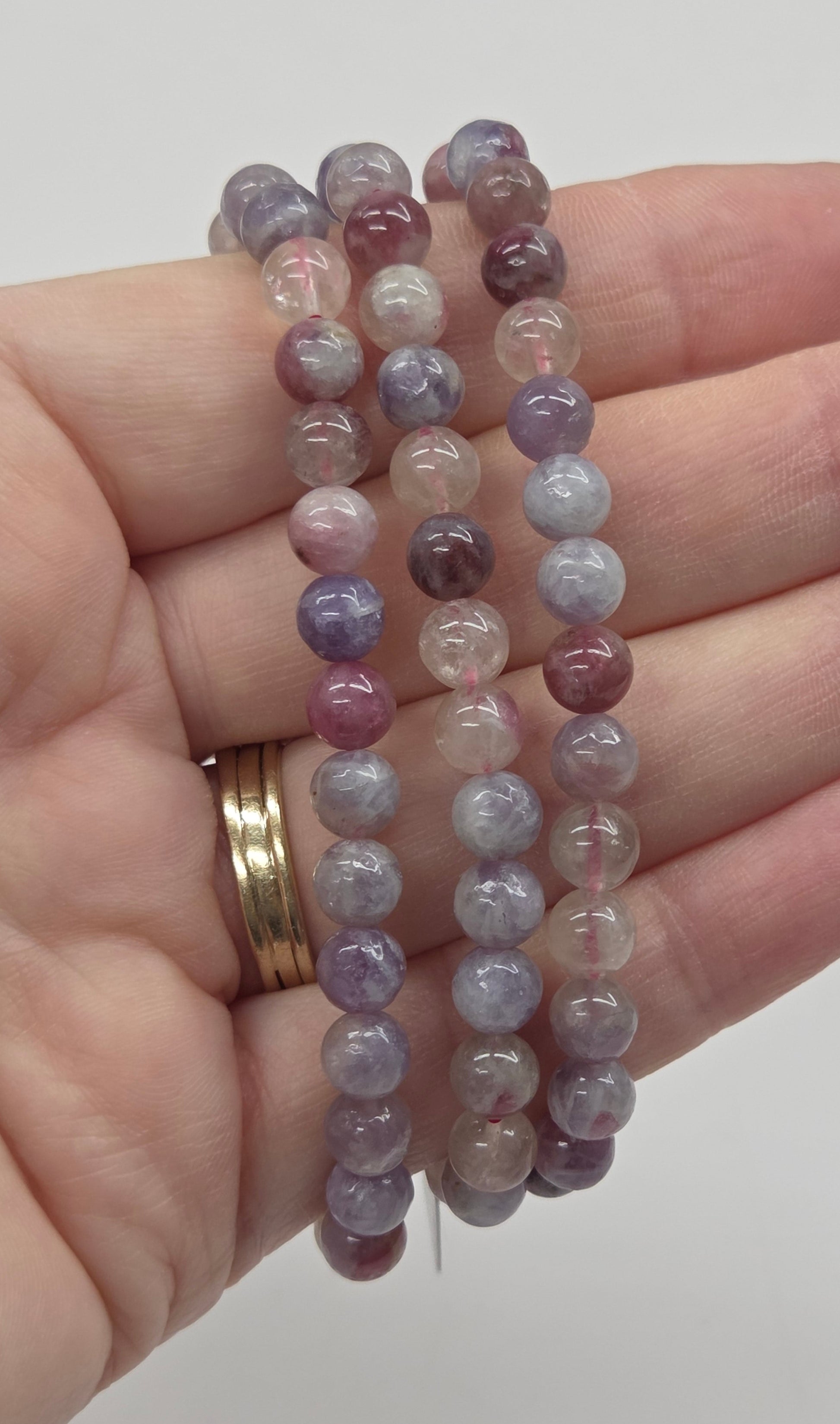 Hand holding three beaded bracelets with a plain background