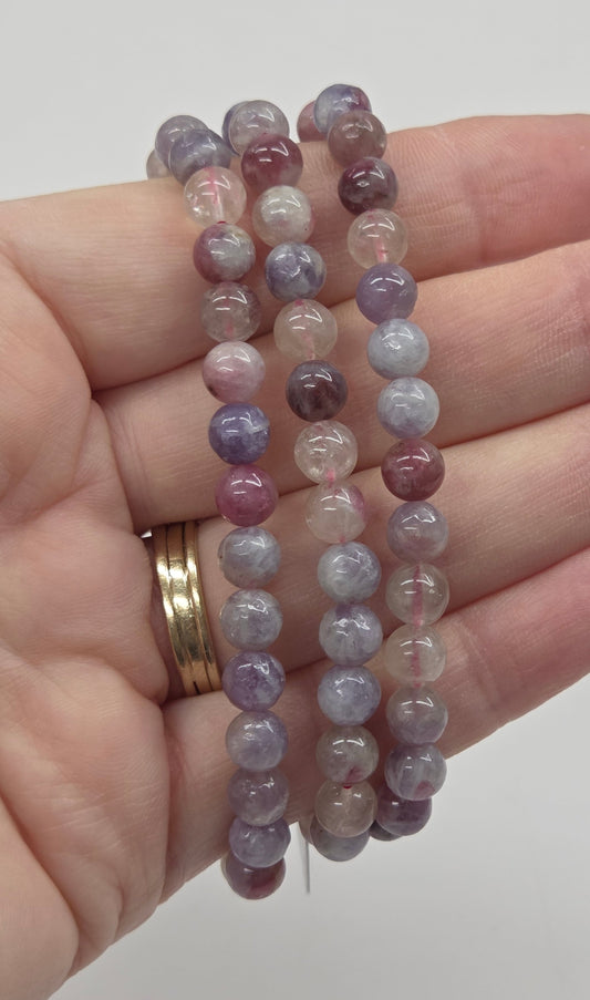 Hand holding three beaded bracelets with a plain background