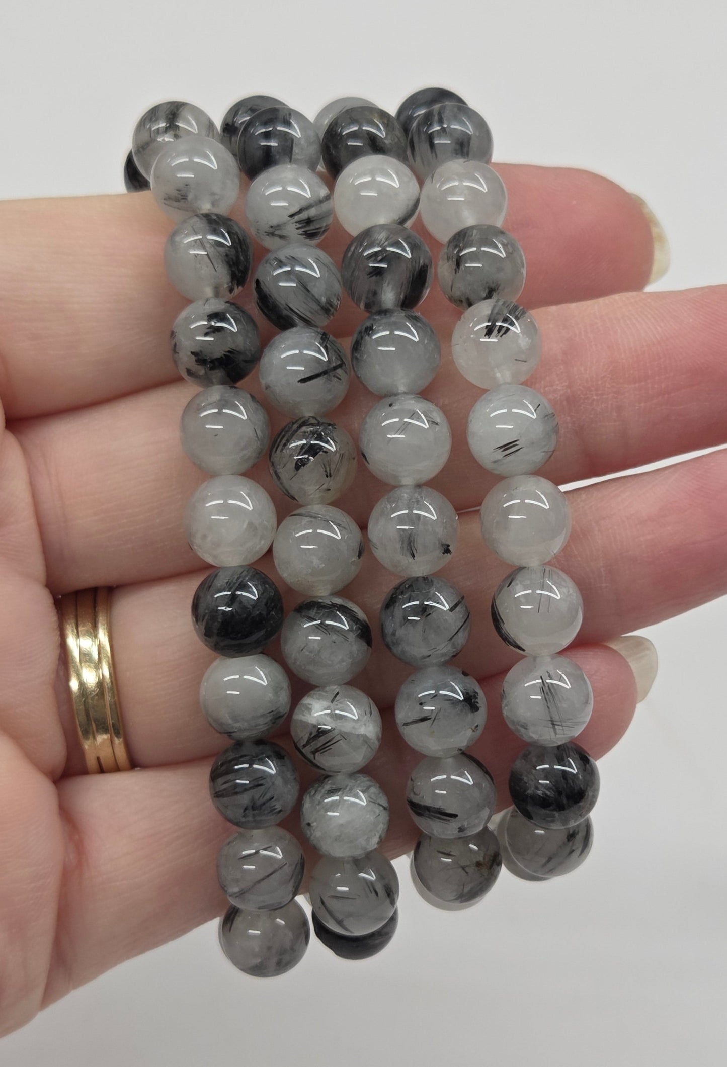 Stack of gray beaded bracelets on a hand against a plain background