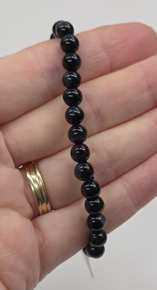 Black beaded bracelet on a hand with a gold ring, against a plain background