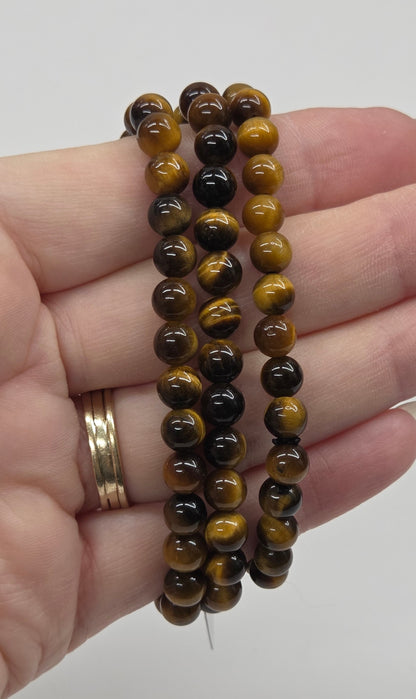 Hand wearing three beaded bracelets on a plain background